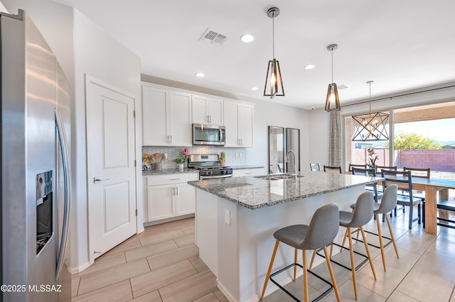 kitchen featuring a sink, decorative backsplash, appliances with stainless steel finishes, light stone countertops, and visible vents