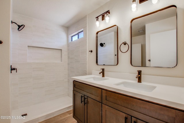 bathroom featuring tiled shower and double vanity
