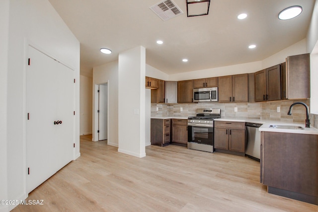 kitchen featuring appliances with stainless steel finishes, a sink, backsplash, light wood-style floors, and light countertops