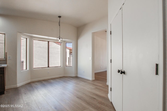 unfurnished dining area with light wood finished floors, baseboards, and vaulted ceiling