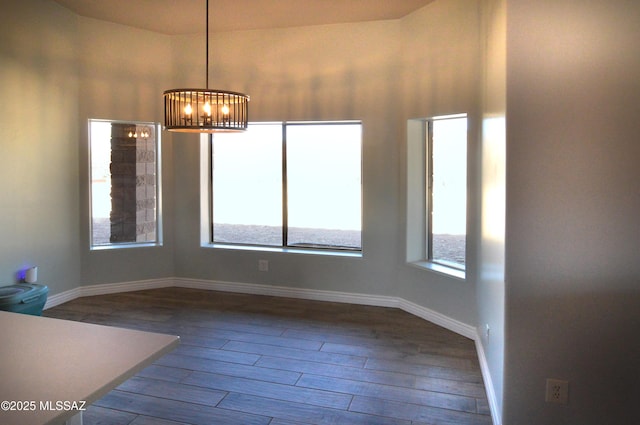 unfurnished dining area featuring baseboards, dark wood-style flooring, and a notable chandelier
