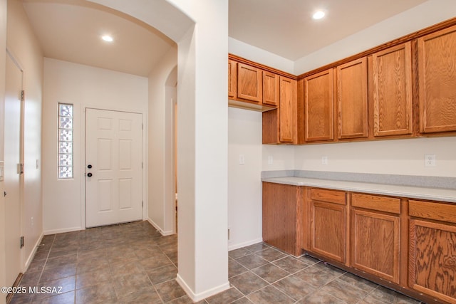 kitchen featuring arched walkways, light countertops, brown cabinetry, and recessed lighting
