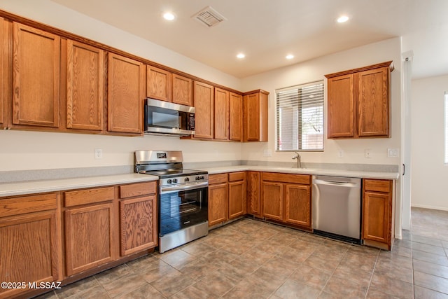 kitchen featuring brown cabinetry, appliances with stainless steel finishes, a sink, and visible vents
