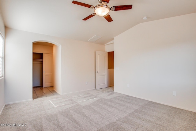 unfurnished bedroom with vaulted ceiling, arched walkways, baseboards, light colored carpet, and ceiling fan