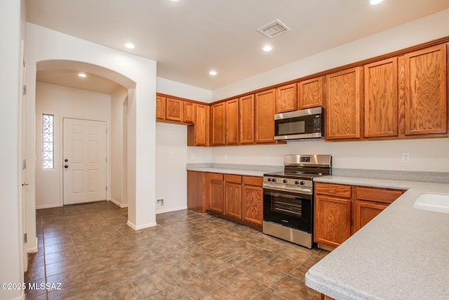 kitchen with brown cabinets, stainless steel appliances, light countertops, visible vents, and arched walkways
