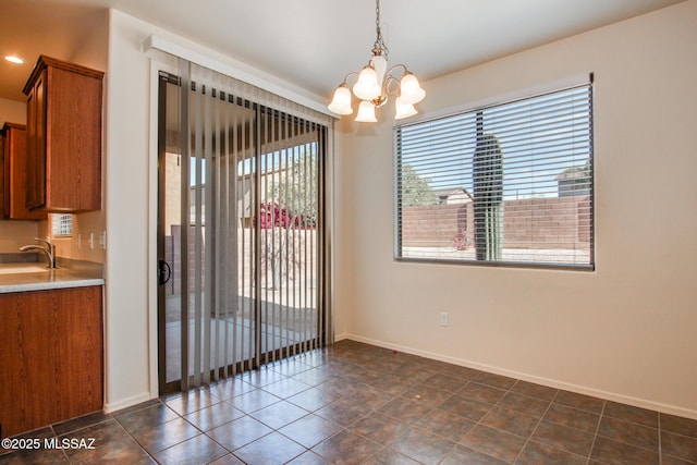 unfurnished dining area featuring dark tile patterned floors, baseboards, a sink, and an inviting chandelier
