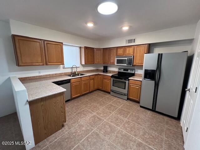 kitchen with stainless steel appliances, light countertops, visible vents, a sink, and brown cabinetry