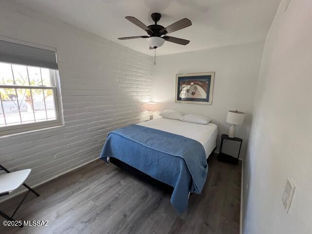 bedroom featuring wood finished floors, brick wall, and a ceiling fan