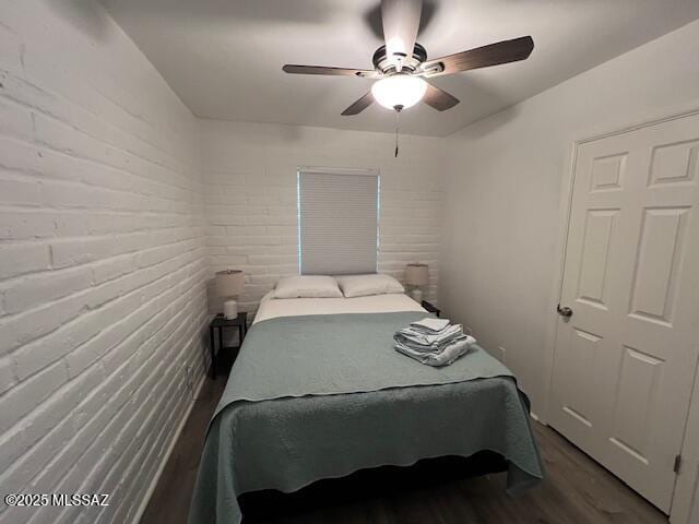 bedroom featuring wood finished floors, brick wall, and a ceiling fan