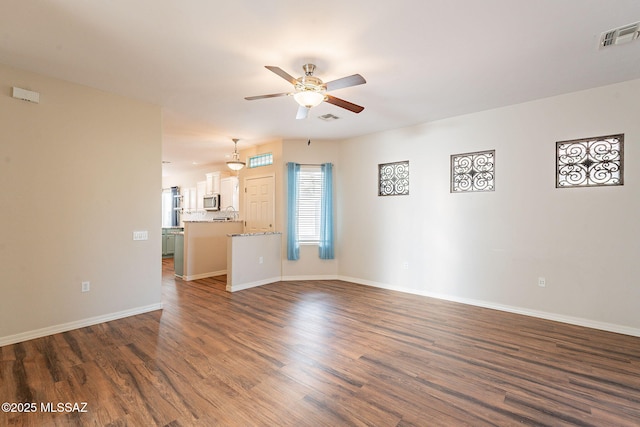 unfurnished living room with visible vents, a ceiling fan, and dark wood-style floors