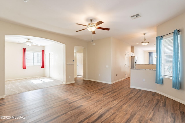 unfurnished living room featuring arched walkways, wood finished floors, and a ceiling fan