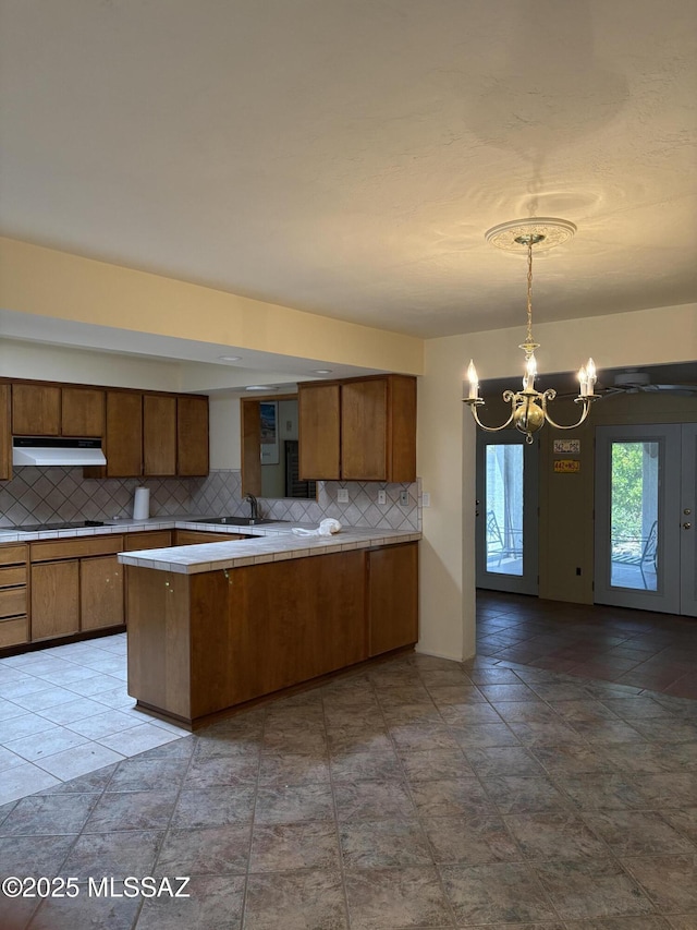 291 E Los Rincones, Green Valley, AZ 85614 - kitchen with tasteful backsplash, a notable chandelier, a peninsula, under cabinet range hood, and brown cabinets