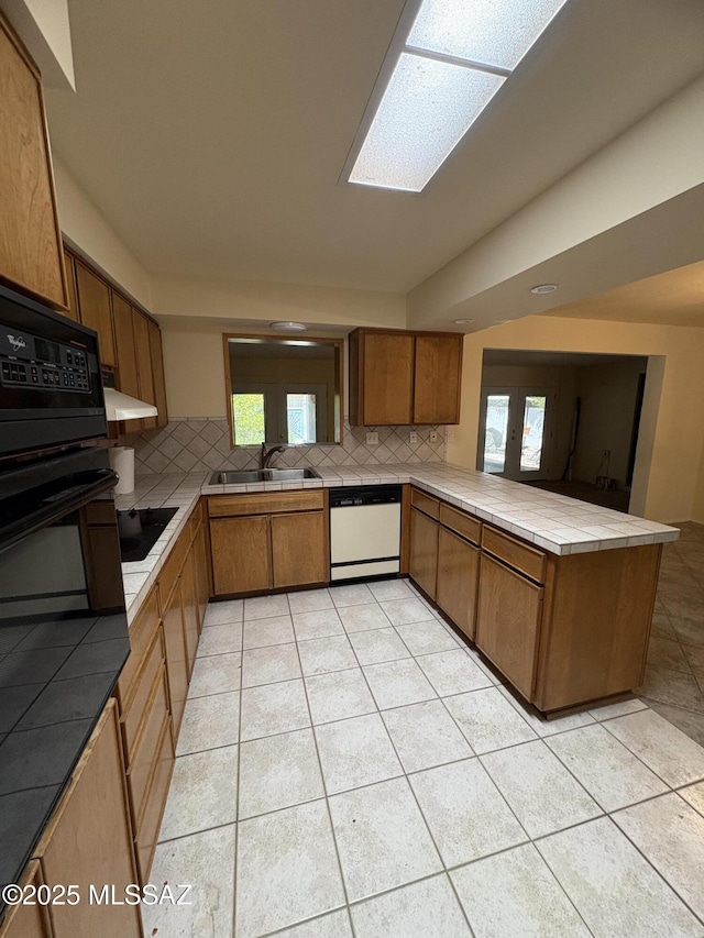 291 E Los Rincones, Green Valley, AZ 85614 - kitchen with brown cabinetry, a peninsula, black appliances, light tile patterned flooring, and a sink