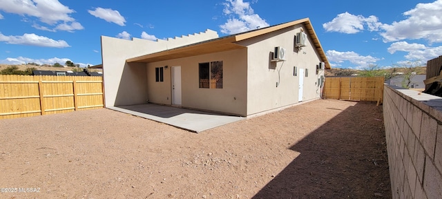 rear view of property with a patio area, a fenced backyard, a wall unit AC, and stucco siding