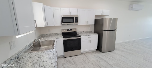 kitchen featuring light stone countertops, a wall unit AC, white cabinets, a sink, and stainless steel appliances