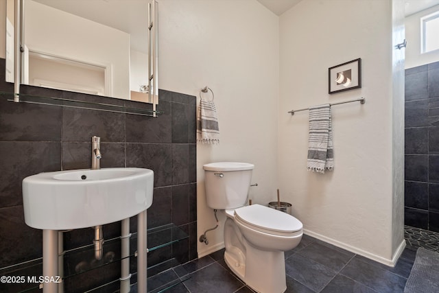 bathroom with baseboards, tile patterned floors, toilet, and tile walls