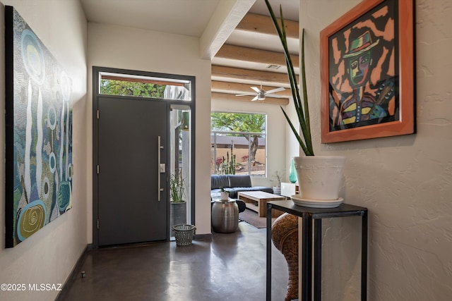 foyer entrance with beamed ceiling, concrete floors, and ceiling fan