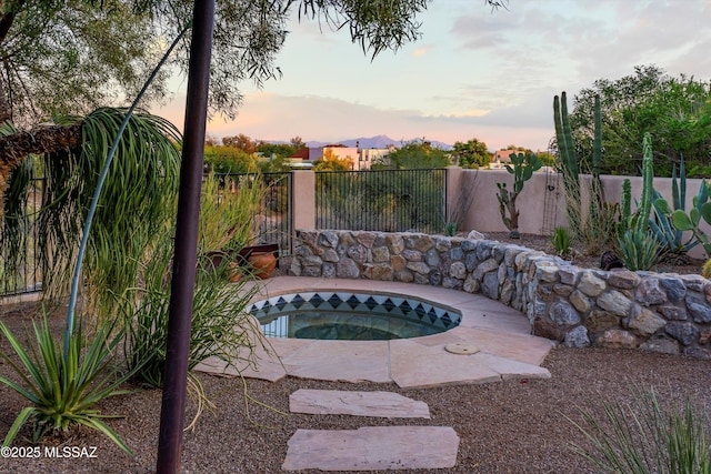 pool at dusk featuring an in ground hot tub and fence