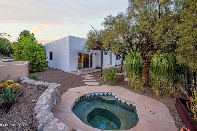 back of house at dusk with an in ground hot tub and stucco siding