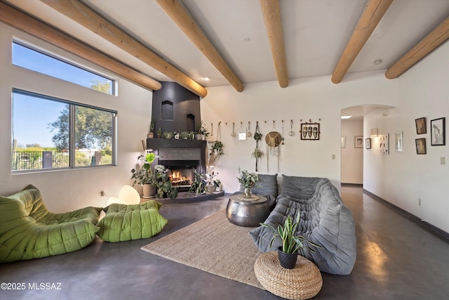 living room featuring beam ceiling, baseboards, a warm lit fireplace, finished concrete floors, and arched walkways