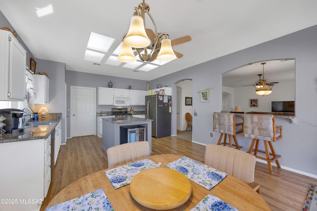 dining room featuring light wood finished floors, baseboards, ceiling fan with notable chandelier, and arched walkways