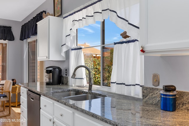 kitchen featuring white cabinetry, dark stone countertops, dishwasher, and a sink