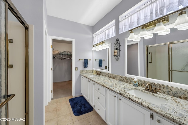 full bath featuring a sink, a shower stall, tile patterned floors, a walk in closet, and double vanity