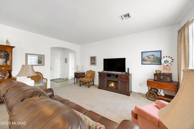 living area with visible vents, light carpet, a warm lit fireplace, and arched walkways