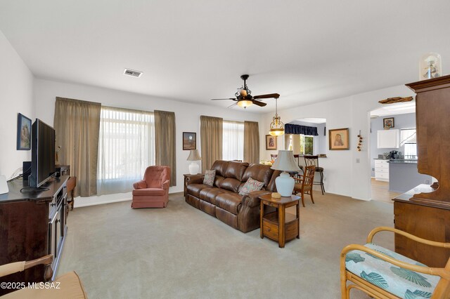 living room featuring arched walkways, visible vents, ceiling fan, and light carpet