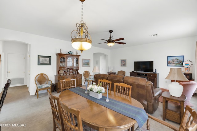 dining area with light colored carpet, visible vents, ceiling fan, and arched walkways