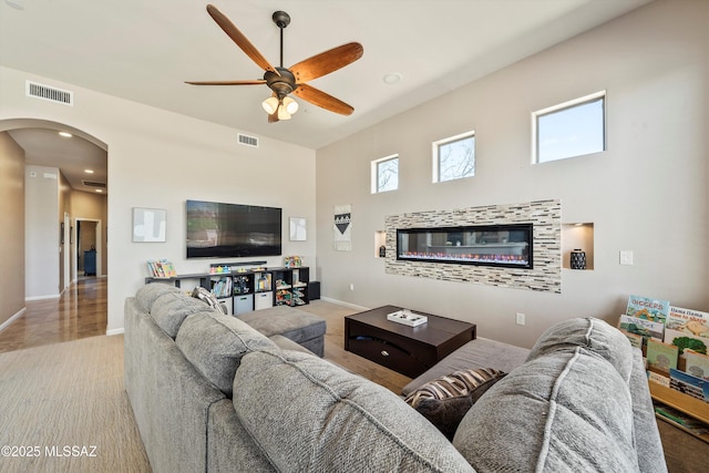 living room with arched walkways, carpet floors, visible vents, and a ceiling fan