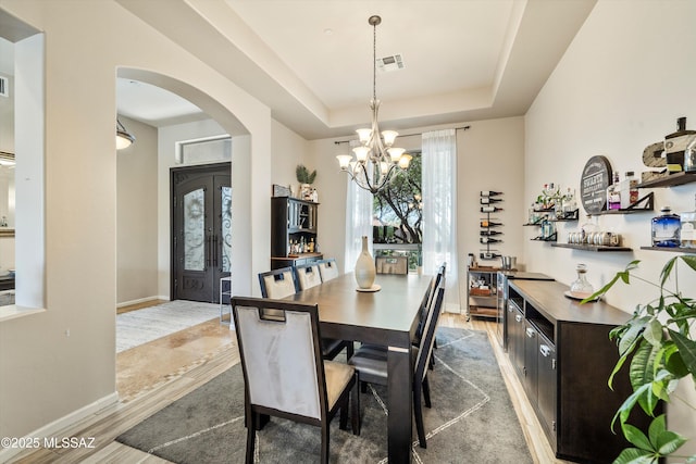 dining room featuring a chandelier, arched walkways, a dry bar, a raised ceiling, and visible vents