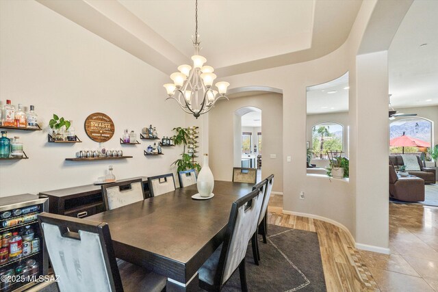 dining area featuring indoor bar, arched walkways, light wood-type flooring, and an inviting chandelier