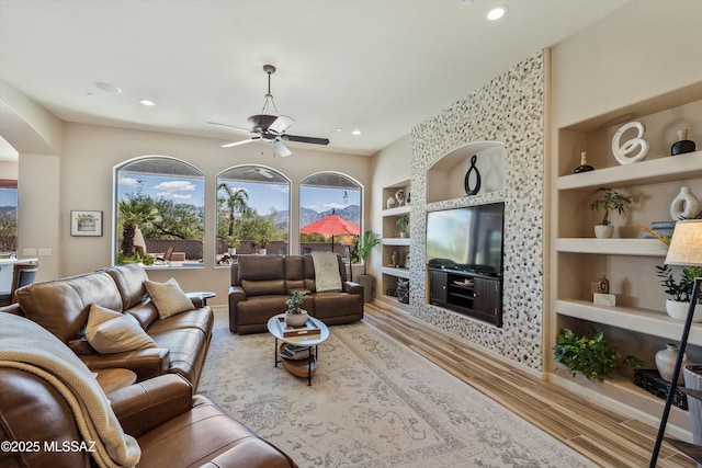 living room with arched walkways, baseboards, built in shelves, wood finished floors, and ceiling fan