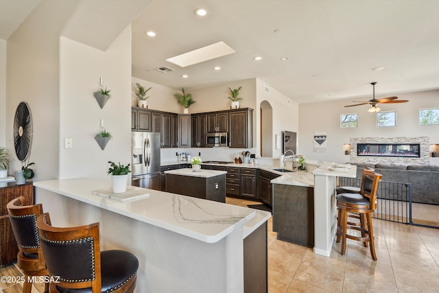 kitchen with a peninsula, a sink, open floor plan, appliances with stainless steel finishes, and a breakfast bar area