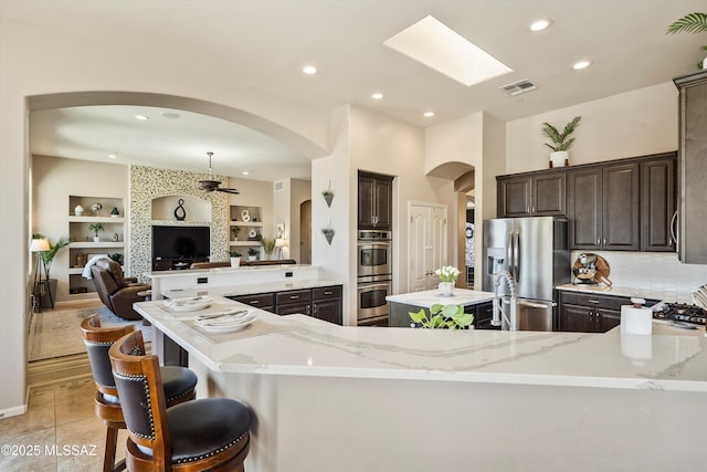 kitchen featuring arched walkways, light stone counters, dark brown cabinets, and stainless steel appliances