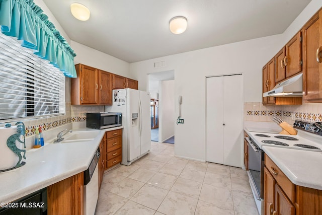 kitchen with under cabinet range hood, white appliances, light countertops, and backsplash