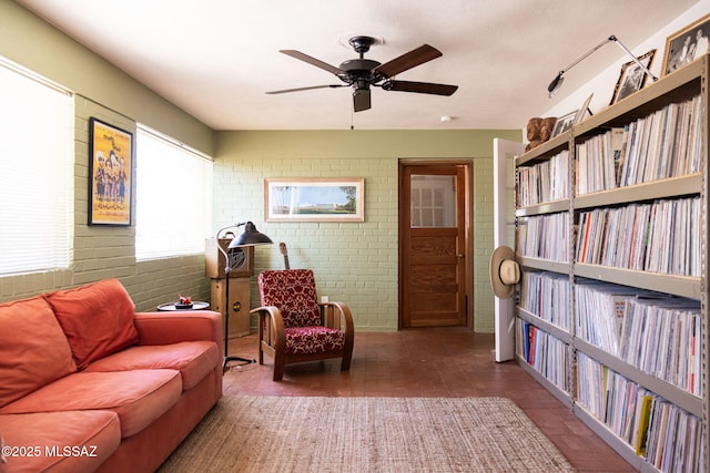 sitting room featuring ceiling fan and brick wall