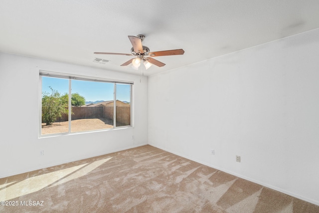 empty room with carpet flooring, a ceiling fan, baseboards, and visible vents
