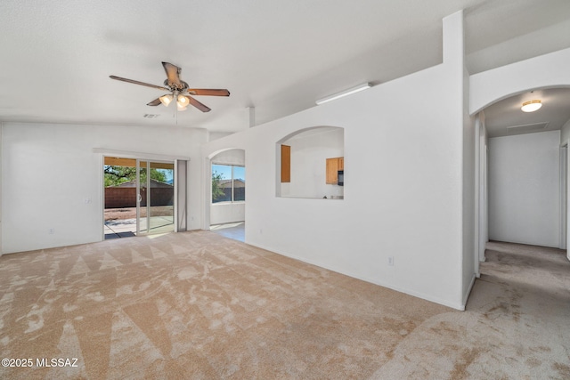 unfurnished room with carpet flooring, a ceiling fan, and arched walkways