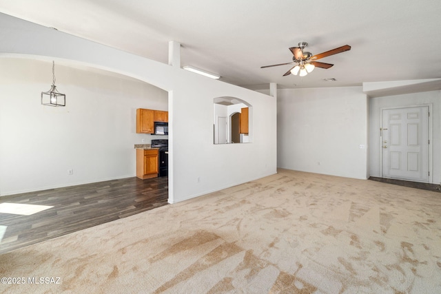 unfurnished living room featuring arched walkways, a ceiling fan, dark carpet, and dark wood-type flooring
