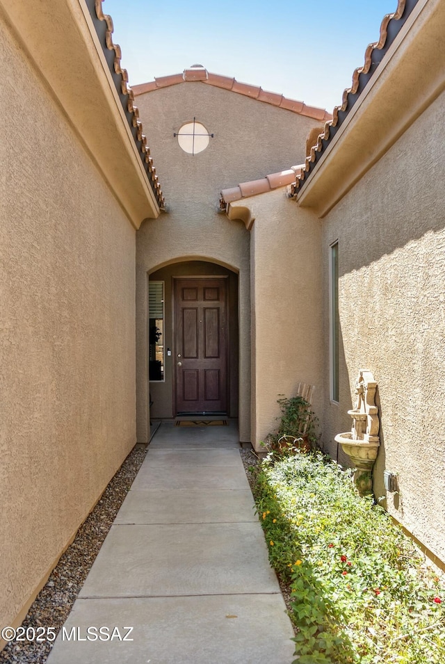 view of exterior entry with a tile roof and stucco siding