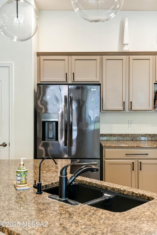 kitchen featuring a sink, stainless steel refrigerator with ice dispenser, and light stone counters