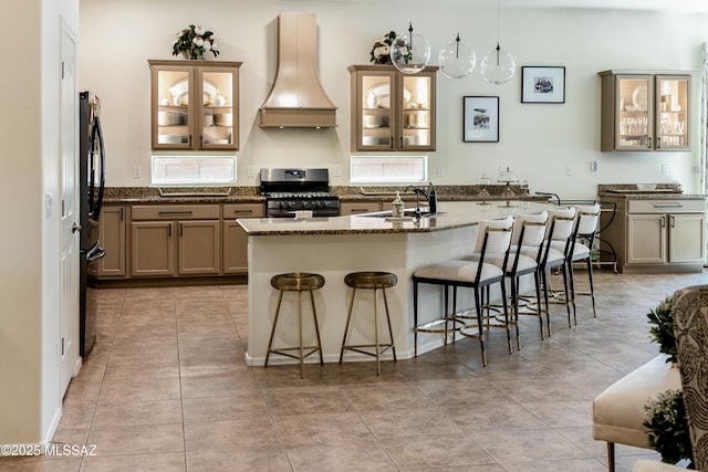 kitchen featuring a sink, premium range hood, gas stove, a kitchen island with sink, and a kitchen bar