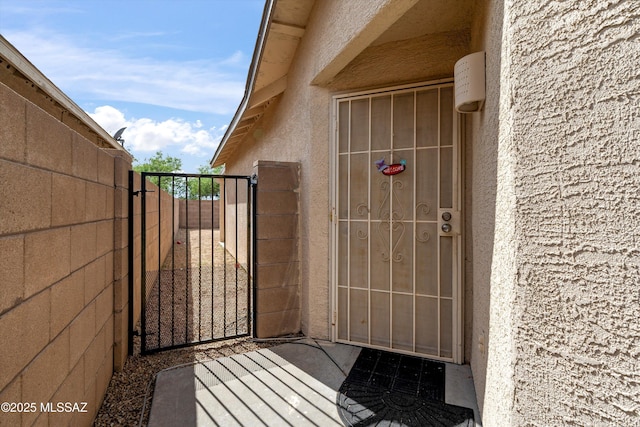 entrance to property featuring stucco siding, fence, and a gate