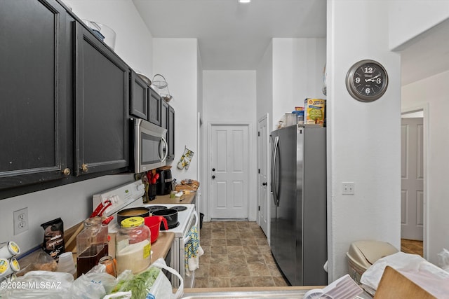 kitchen with dark cabinets, appliances with stainless steel finishes, stone finish flooring, and light countertops