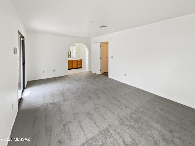spare room featuring arched walkways, baseboards, and carpet floors
