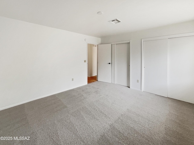 unfurnished bedroom with two closets, carpet flooring, and visible vents