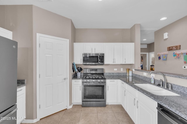 kitchen with light tile patterned floors, stone counters, white cabinets, appliances with stainless steel finishes, and a sink