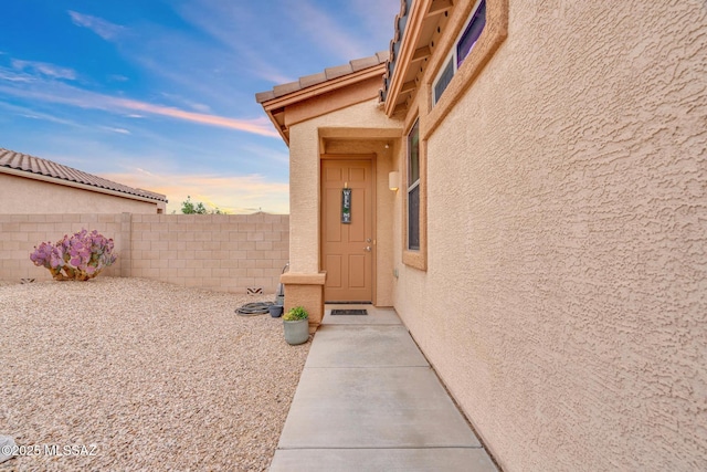 exterior entry at dusk with stucco siding and fence